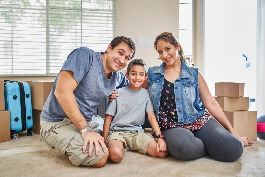Family smiling on the floor of their new home surrounded by moving boxes